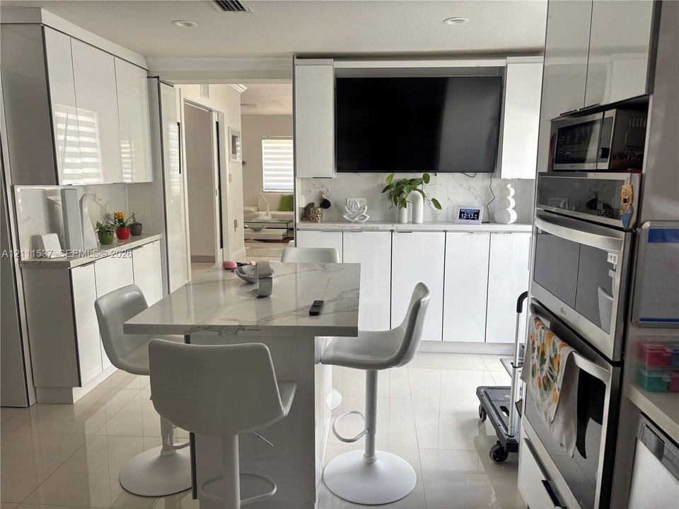 High-gloss white cabinetry, integrated stone-finish countertops, stainless steel wall-mounted oven and microwave, and large-format tile flooring