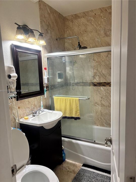 Bathroom featuring stone-tile walls, sliding glass shower enclosure, vanity with integrated basin, dark wood-finish cabinetry, and three-light wall-mounted fixture