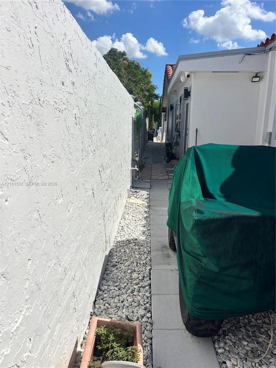 Exterior side walkway featuring a stucco privacy wall, stone ground cover, and concrete paver pathway
