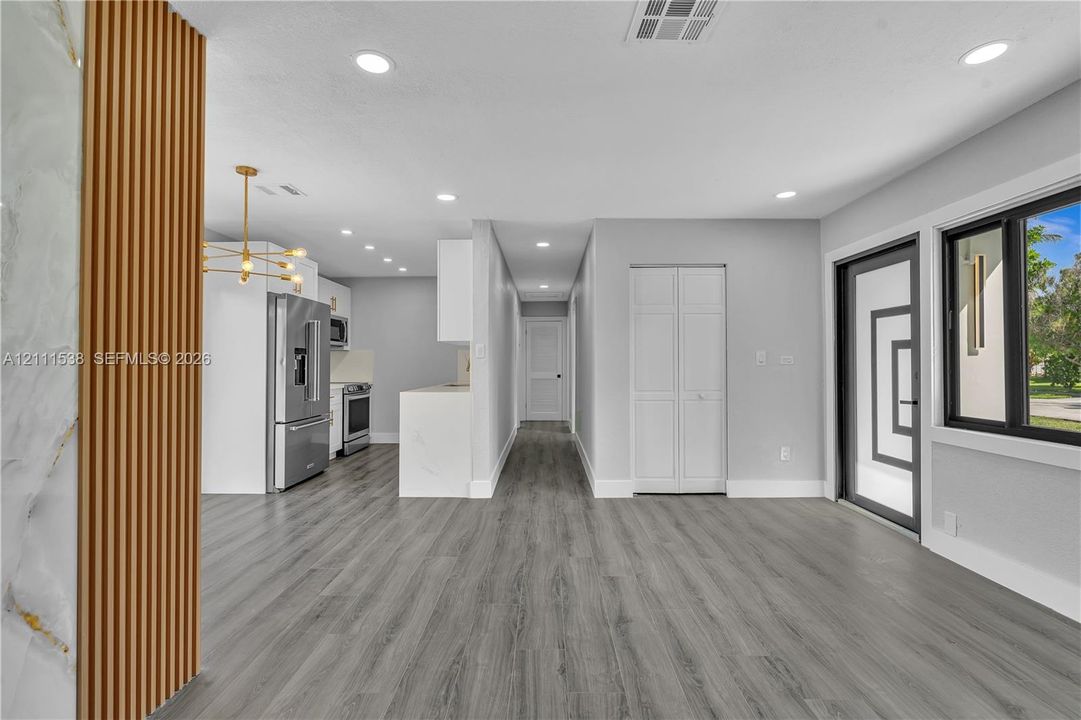 Open-concept interior featuring wood-finish flooring, recessed lighting, a modern multi-light chandelier, a stone-accented slat wall feature, and a kitchen equipped with stainless steel appliances