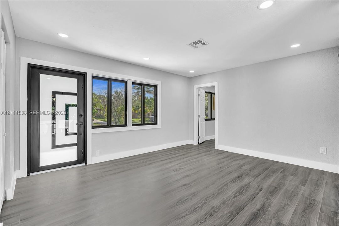 Interior space featuring wood-finish flooring, recessed lighting, a full-glass entry door with a dark frame, and multi-pane windows with dark casing
