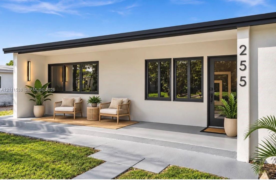 Exterior featuring smooth white stucco finish, dark-framed windows, integrated exterior wall sconce, concrete porch, and front entry door with glass panel