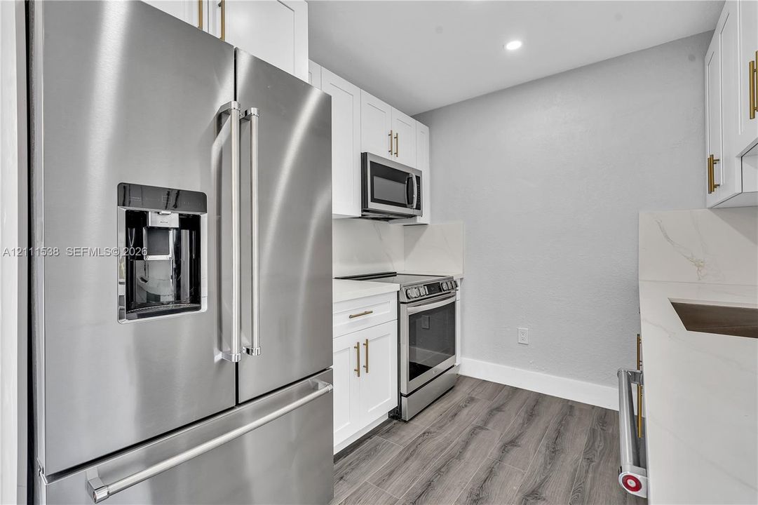 Kitchen featuring stainless steel appliances, white cabinetry with gold-tone hardware, stone-finish countertops, and wood-finish flooring