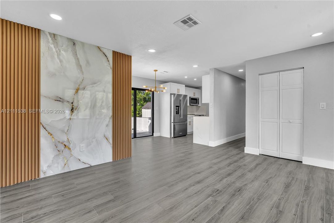 Interior featuring wood-finish flooring, a decorative accent wall with vertical wood slats and a polished stone-finish center panel, recessed lighting, and stainless steel kitchen appliances