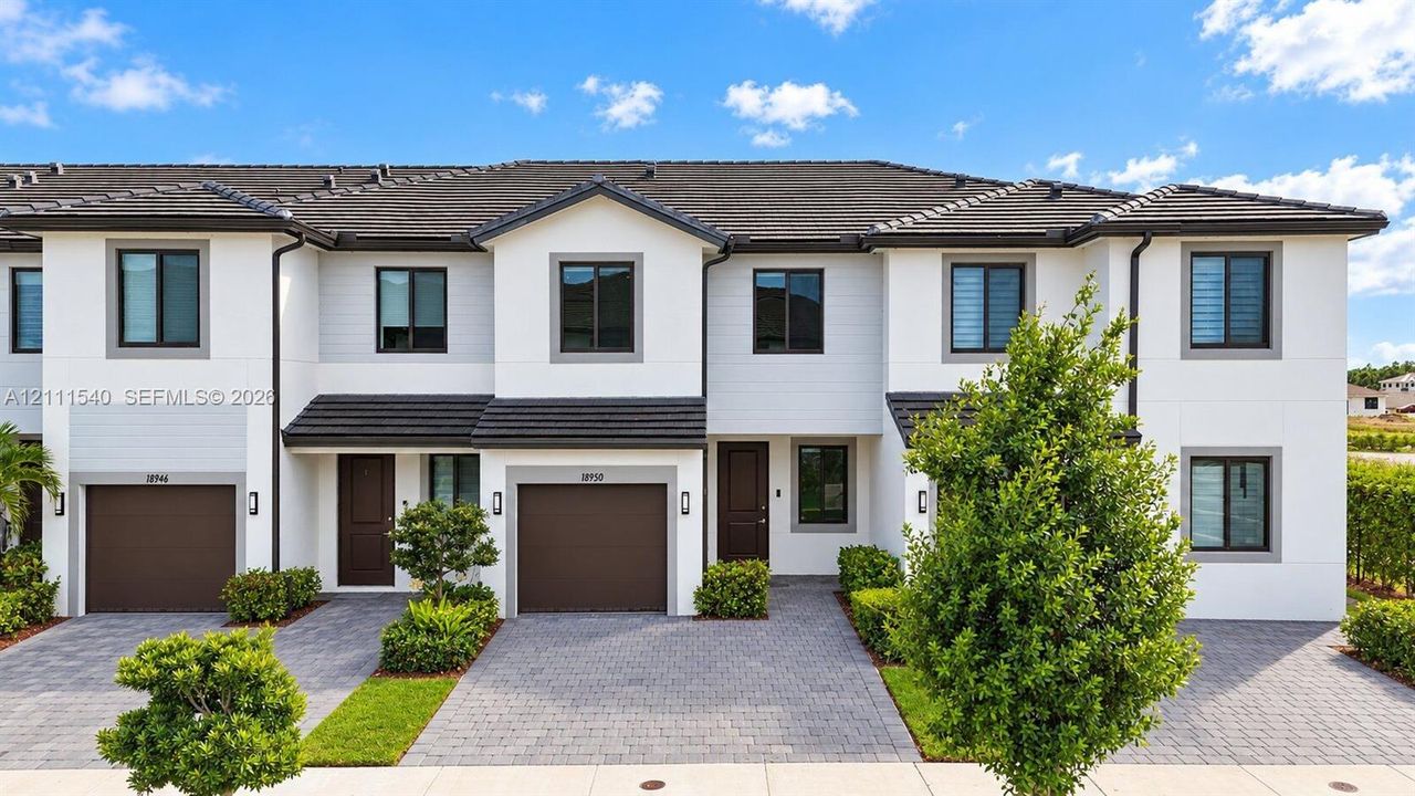 Multi-story townhome exterior featuring crisp white siding, dark-toned tile roofing, paved driveways, and attached garage entries