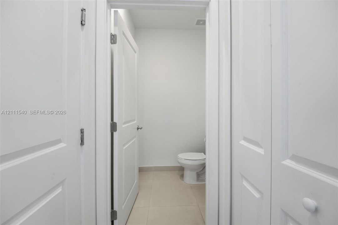 Neutral interior featuring white two-panel doors, neutral large-format floor tile, and a porcelain toilet
