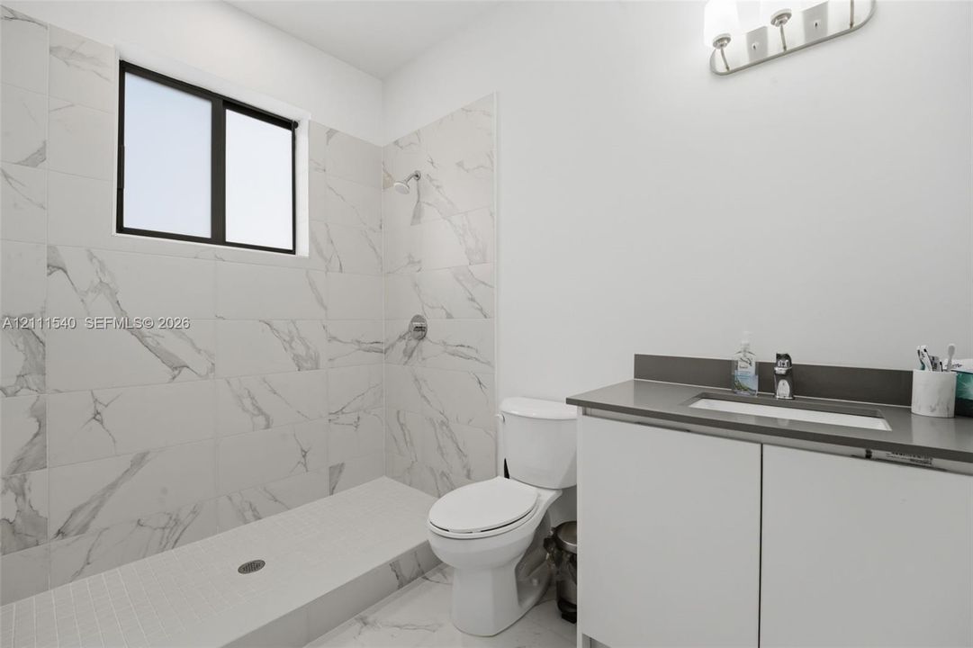 Bathroom featuring a walk-in shower with large-format stone-patterned tile, a vanity with a solid-surface countertop and integrated sink, and wall-mounted vanity lighting