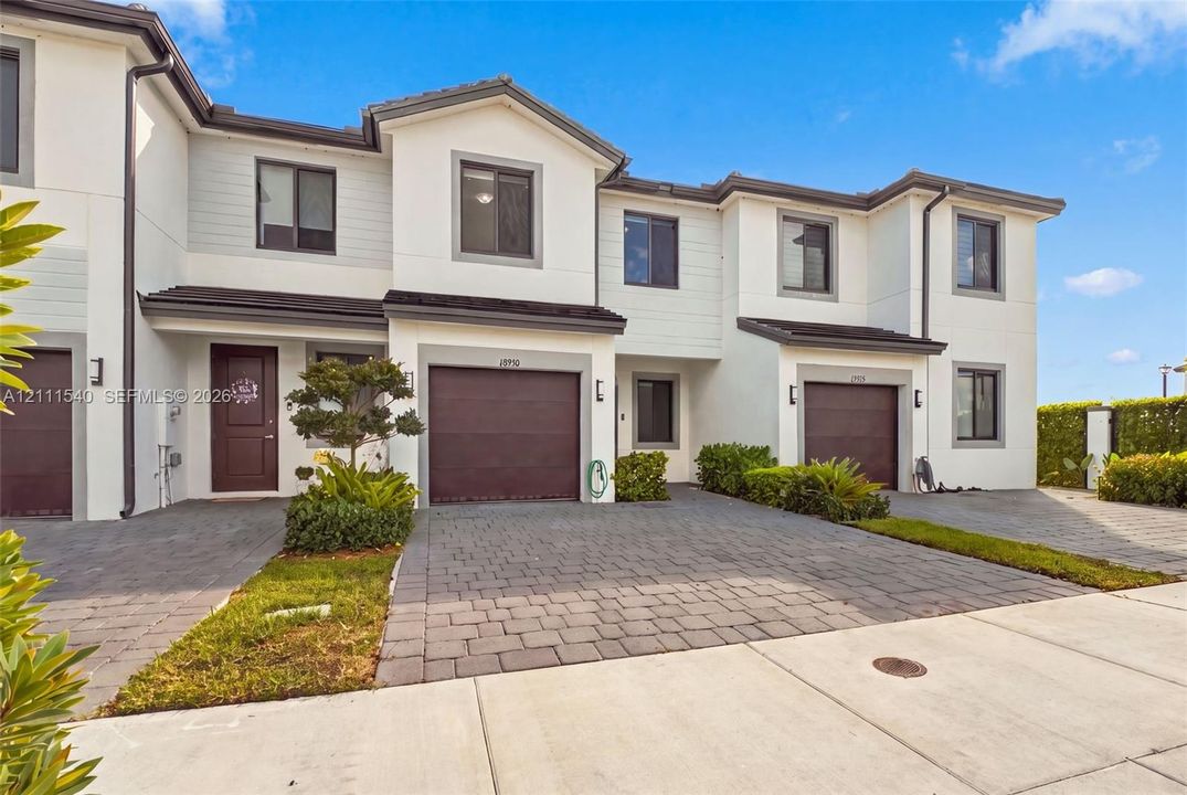 Multi-story townhouse exterior featuring white stucco and horizontal siding, paver-stone driveway, and attached single-car garage with dark-toned door