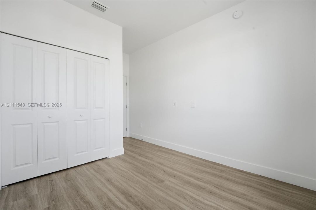 Room featuring wood-finish flooring, white walls, and a white bi-fold closet door