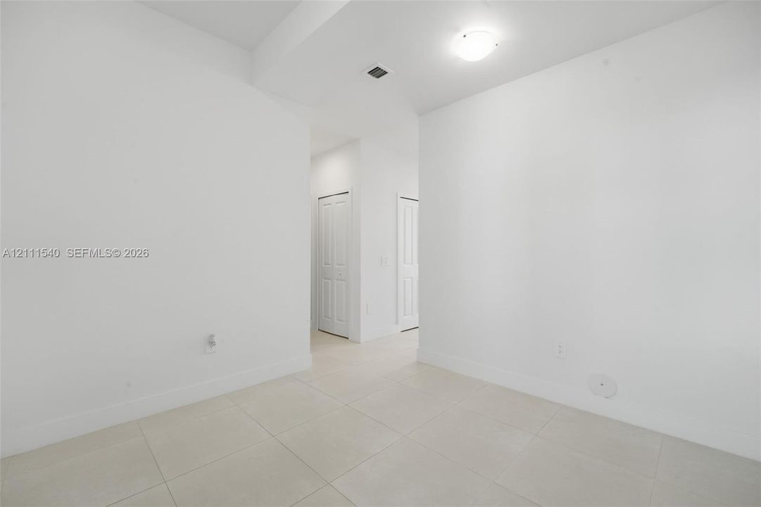 Neutral interior space featuring large-format ceramic tile flooring, crisp white walls, and two multi-panel interior doors