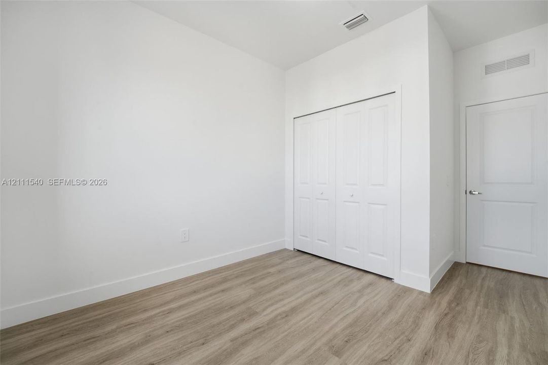 Neutral-toned room featuring wood-finish flooring, a double-panel closet, and a white interior door with metallic hardware