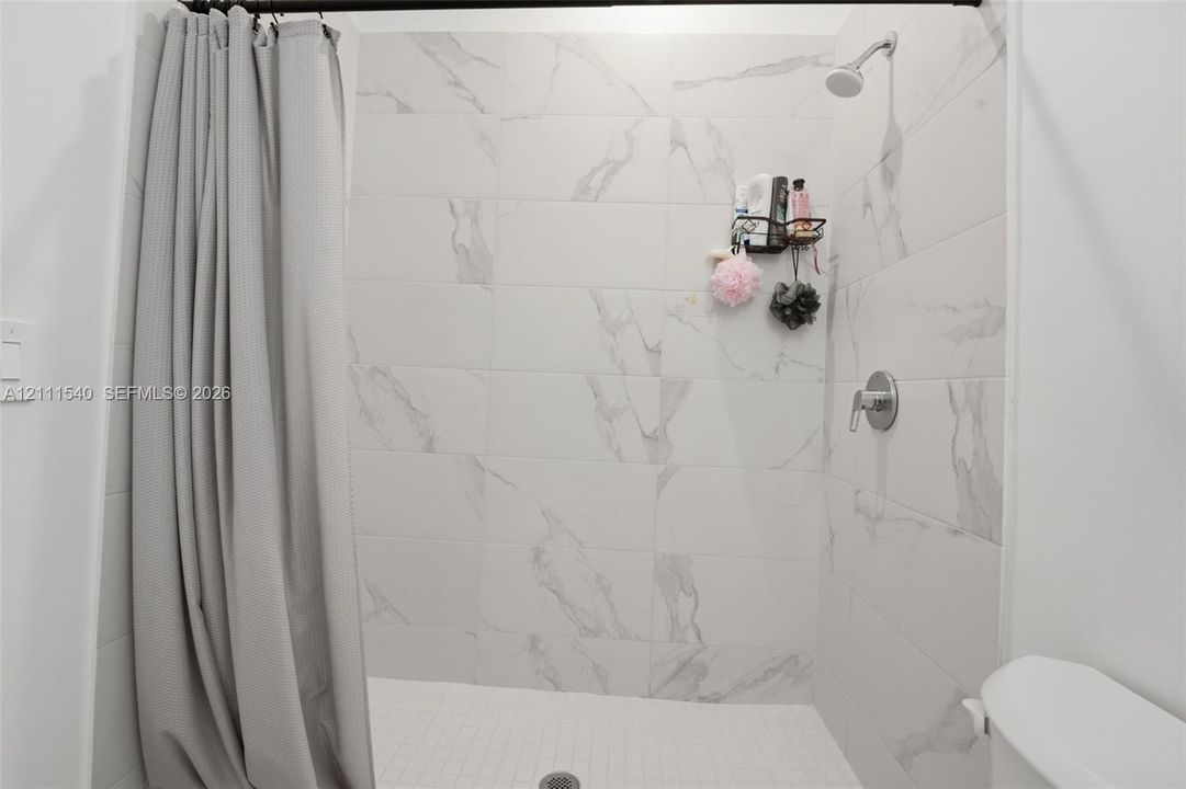 Shower enclosure featuring large-format light-toned stone-finish wall tile with prominent veining, a wall-mounted showerhead, and a single-handle pressure balance valve