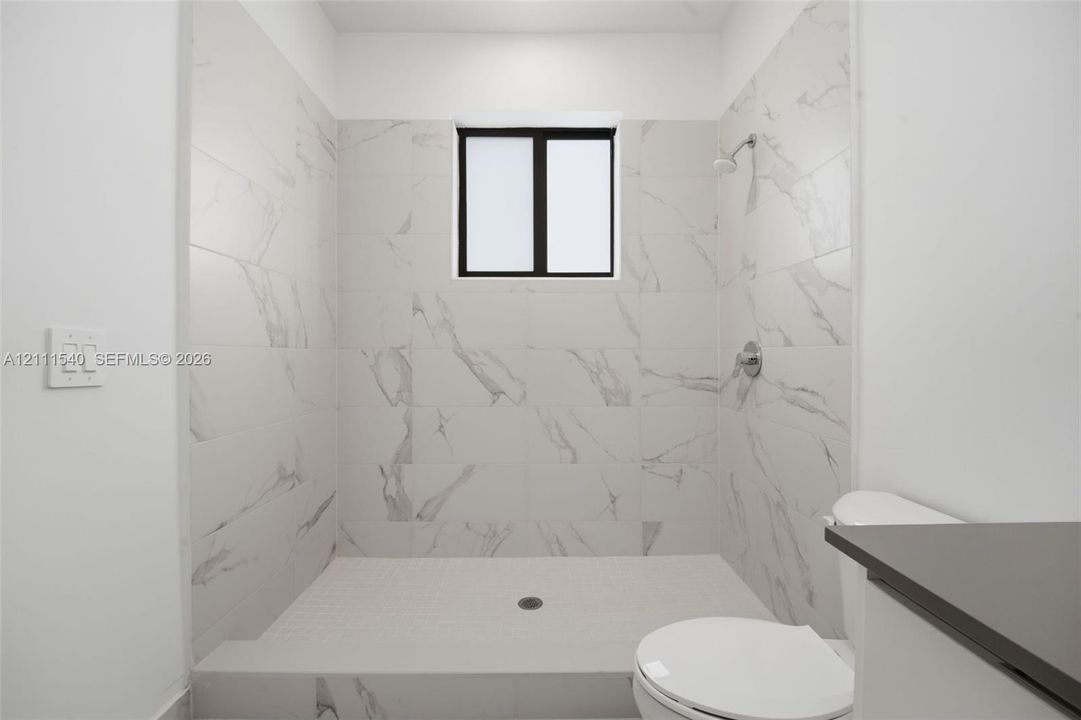 Walk-in shower featuring floor-to-ceiling stone-finish tile surround, a built-in shower head, and a privacy window
