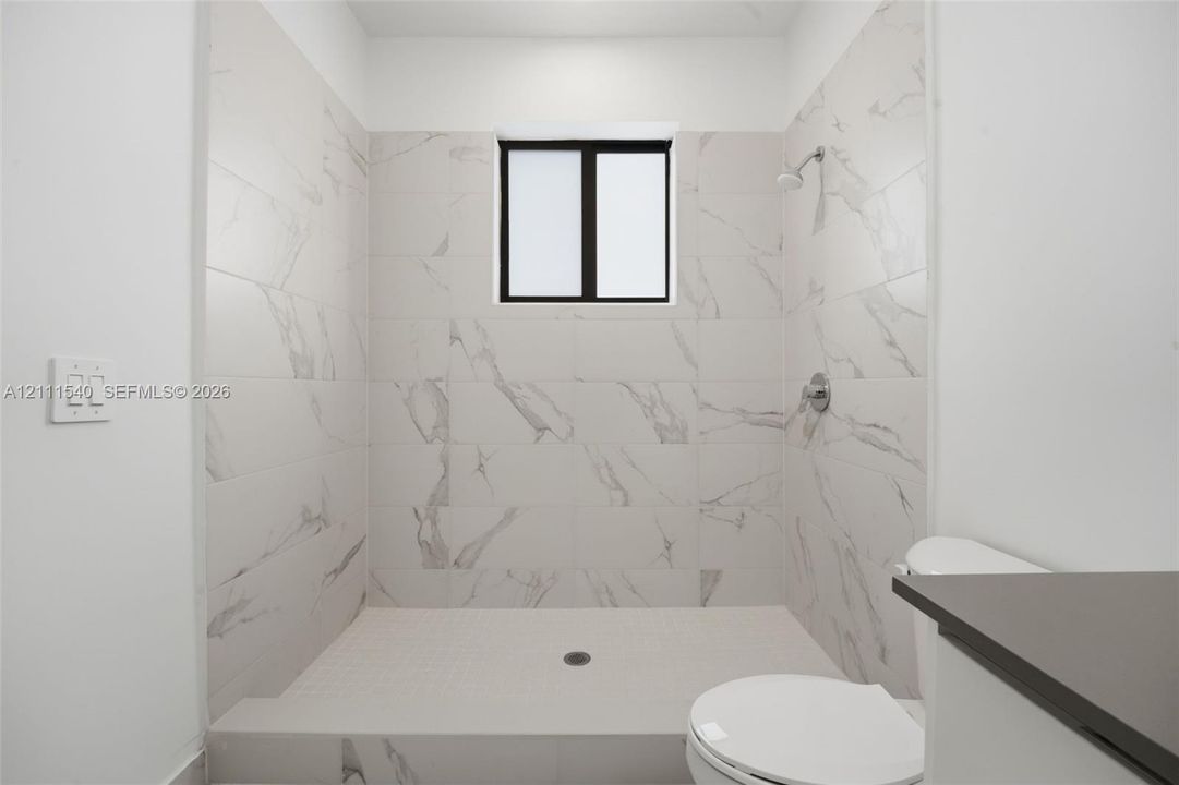 Walk-in shower enclosure featuring large-format stone-patterned tile walls, fixed window, chrome shower fixture, and built-in shower floor
