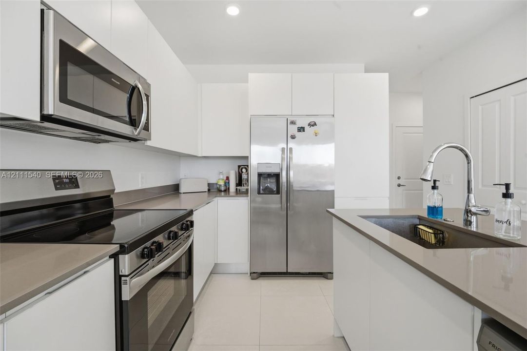 Kitchen featuring flat-panel white cabinetry, stainless steel appliances, quartz countertops, an undermount sink with a gooseneck faucet, and tile flooring