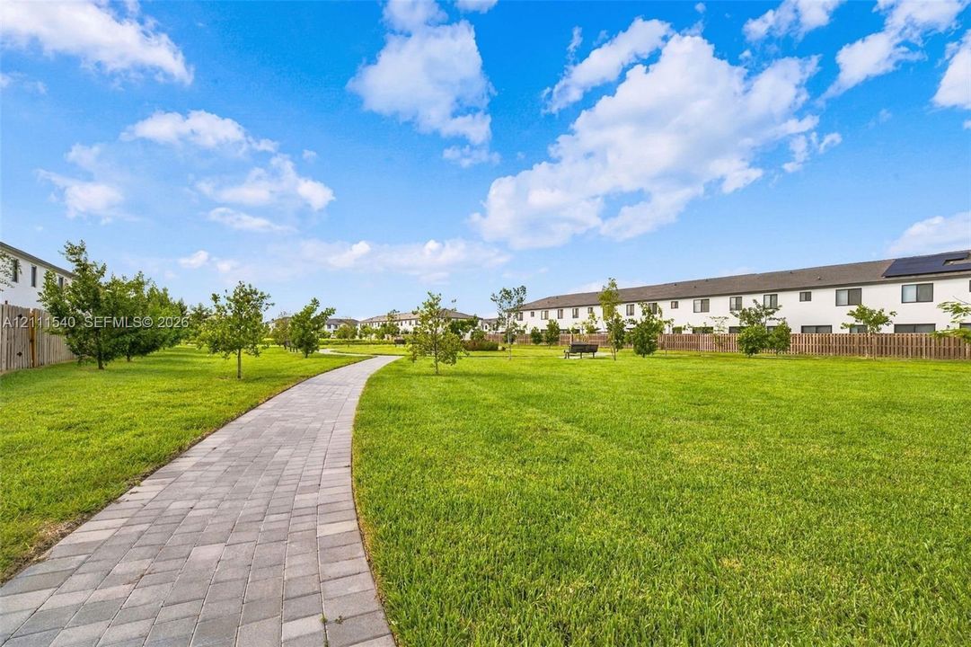 Expansive common area featuring a manicured lawn, paver stone walkway, and mature landscaping