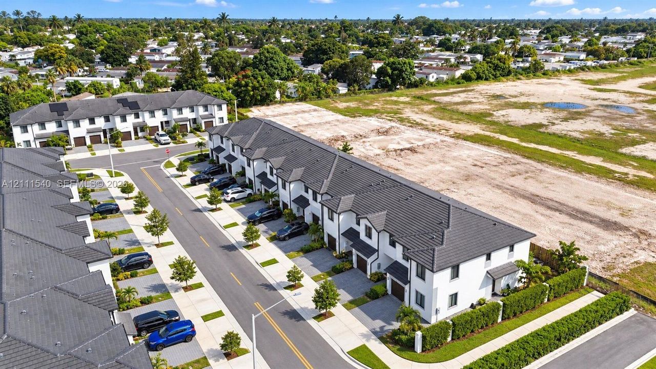 Multi-story townhomes featuring white stucco exteriors, dark tiled roofs, integrated garage bays, and paved driveways