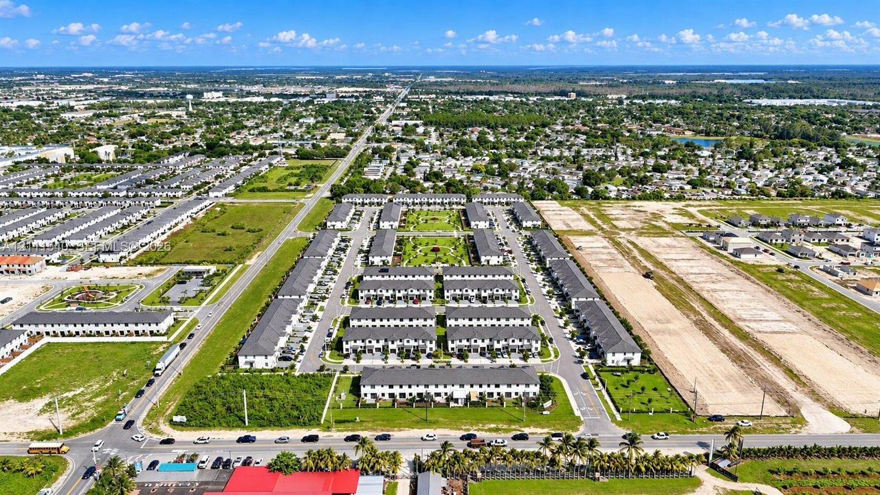 Aerial perspective of a multi-unit residential community featuring paved access roads, central green space, structured landscaping, and surface parking areas