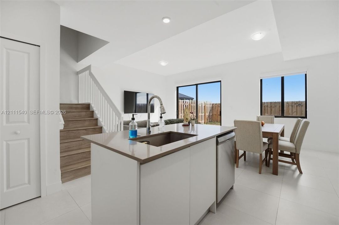Kitchen island with stone-surface countertop, stainless steel undermount sink, wood-finish stairs with white railing, and sliding glass doors