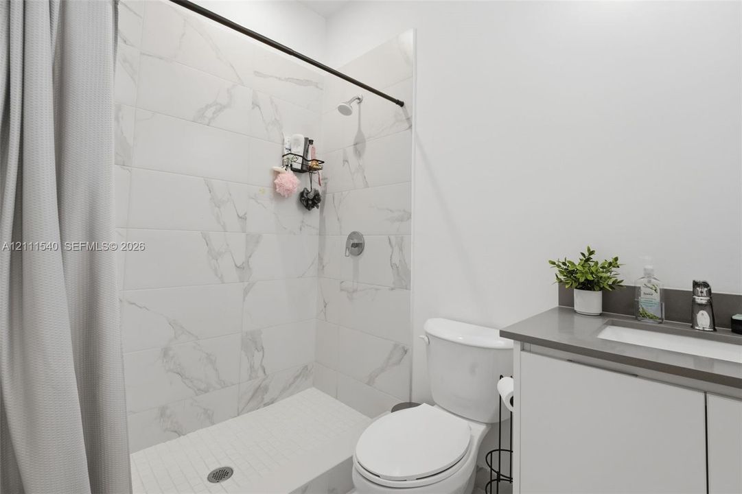 Shower enclosure featuring large-format veined tile surround, matte black shower hardware, and vanity with stone-finish countertop and integrated sink