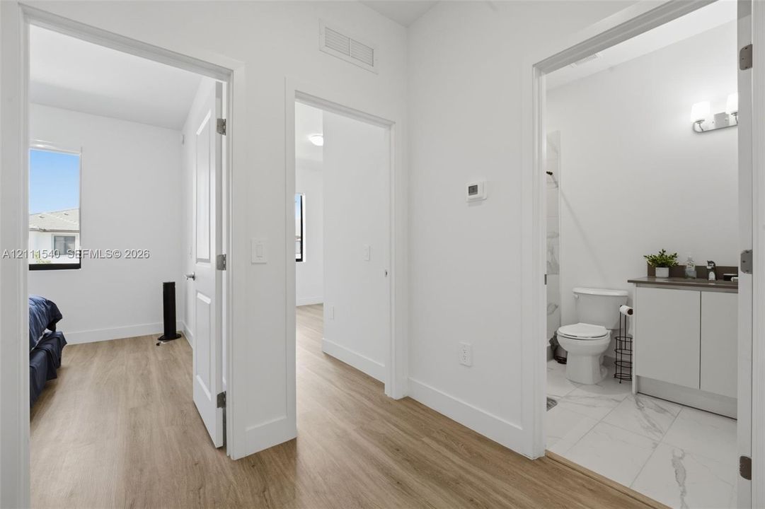 Wood-finish flooring throughout, white interior doors, and a bathroom featuring a vanity with a countertop, a wall-mounted light fixture, and tile flooring