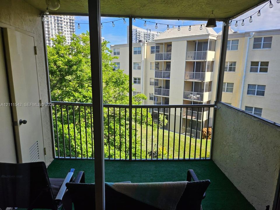 Screened-in balcony featuring metal railings, artificial turf flooring, and a storage closet