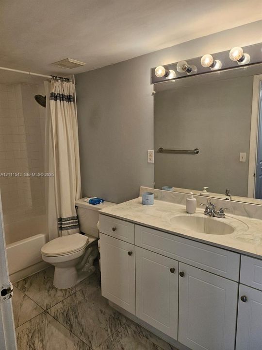 Bathroom featuring a vanity with stone-finish countertop, integrated oval basin, white shaker-style cabinetry, large wall-mounted mirror, and tile flooring