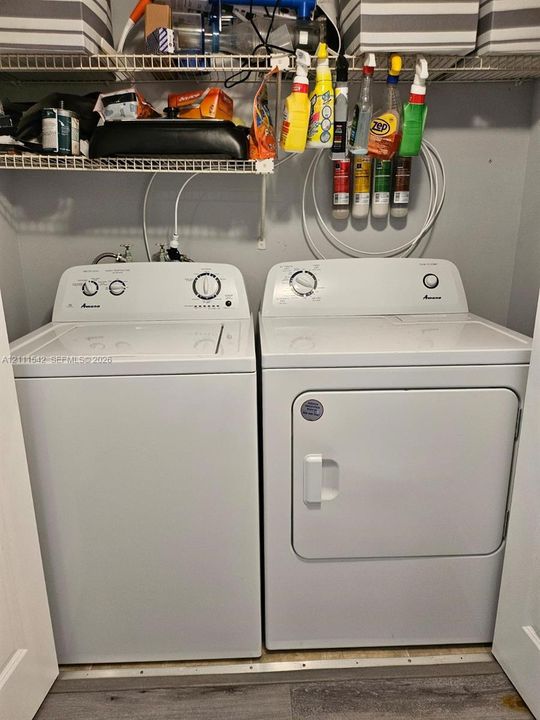 Dedicated laundry space featuring white top-load washer and front-load dryer units, complemented by integrated wire shelving and wood-finish flooring