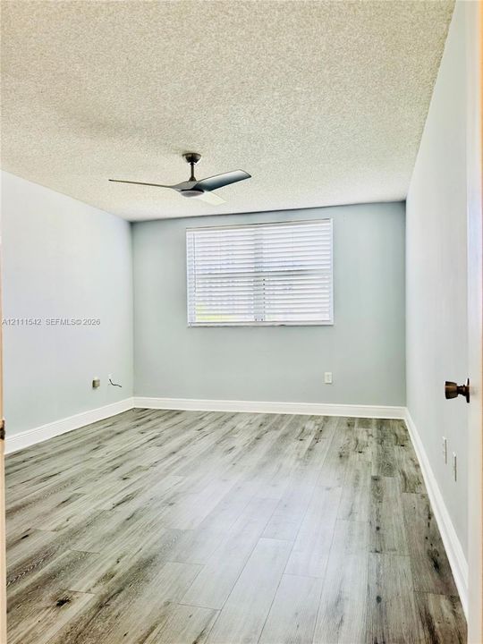 Interior space featuring wood-finish flooring, a matte black ceiling fan, and a single window with horizontal blinds