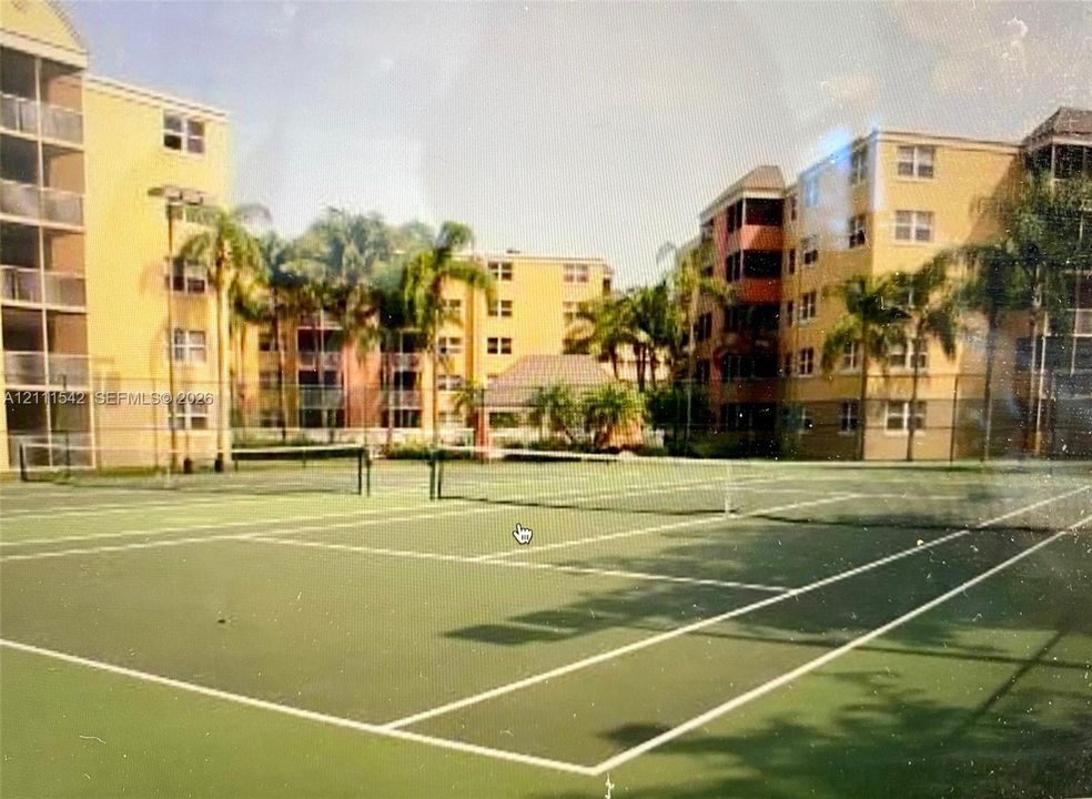 Tennis court featuring a hard surface, perimeter fencing, and mature palm trees