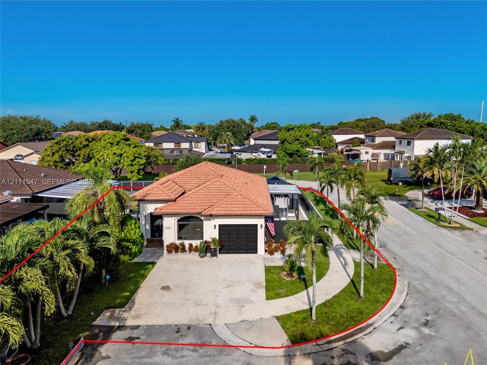 Corner lot exterior featuring a hip roof with clay tiles, arched window detailing, concrete driveway, and mature landscaping