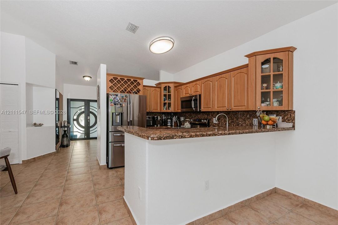Kitchen featuring wood cabinetry with glass-panel upper cabinets, integrated wine storage, stone-finish countertops, and tile flooring