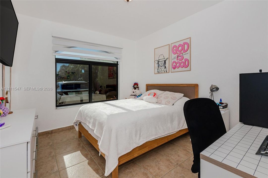 Bedroom featuring neutral wall paint, tile flooring, and a large window with integrated roller shades