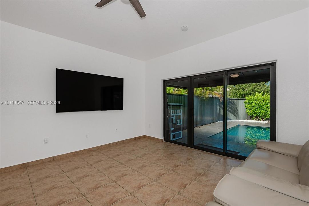 Interior space featuring tile flooring, ceiling fan, and multi-panel sliding glass doors providing external exposure to a swimming pool and fenced perimeter