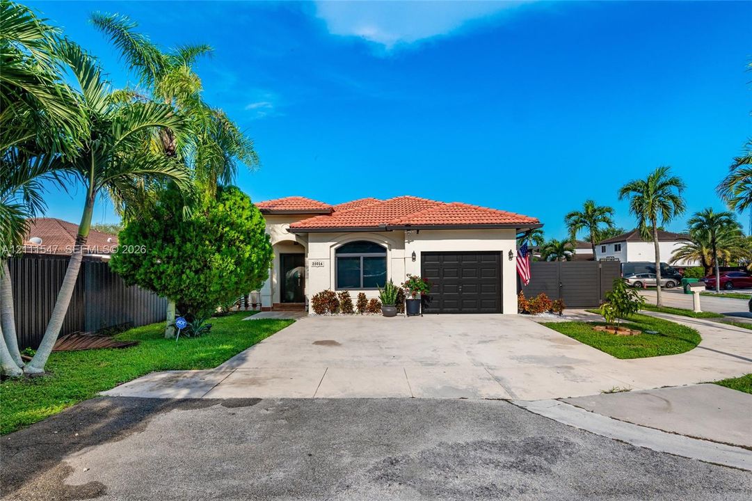 Single-story residence featuring a tile roof, stucco exterior, attached garage with a multi-panel door, concrete driveway, and mature landscaping