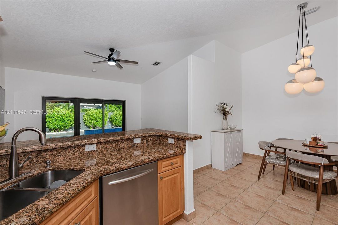 Kitchen featuring stone countertops, stainless steel undermount sink with arched faucet, stainless steel dishwasher, vaulted ceiling with integrated fan, and multi-globe chandelier lighting