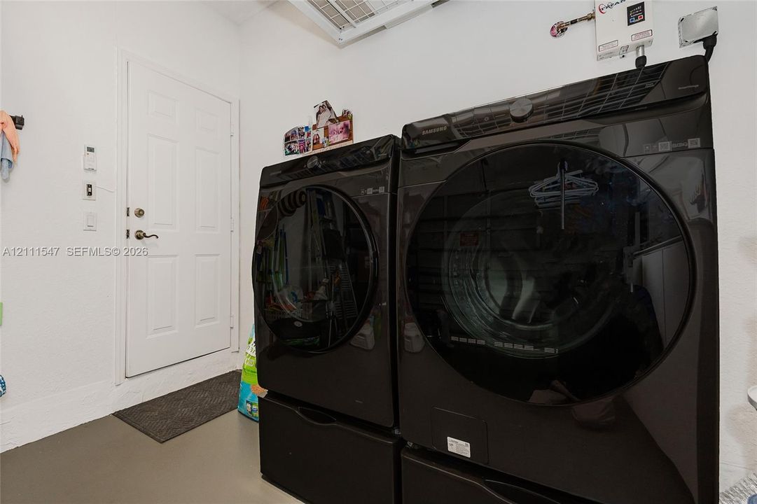 Utility area featuring dark-finished front-load laundry appliances with pedestal bases and a solid-core entry door