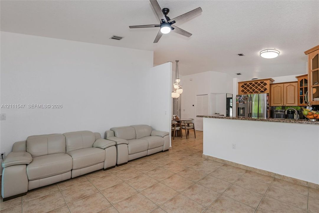Ceramic tile flooring, kitchen featuring wood cabinetry with integrated wine rack, stone-finish countertops, ceiling fan with integrated lighting, and multi-pendant light fixture