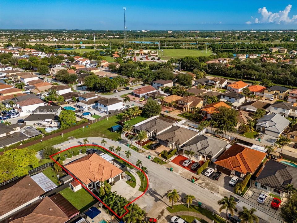 Aerial view of a residential property featuring a clay-tile roof, paved driveway, two-car garage, and established perimeter landscaping situated on a corner lot