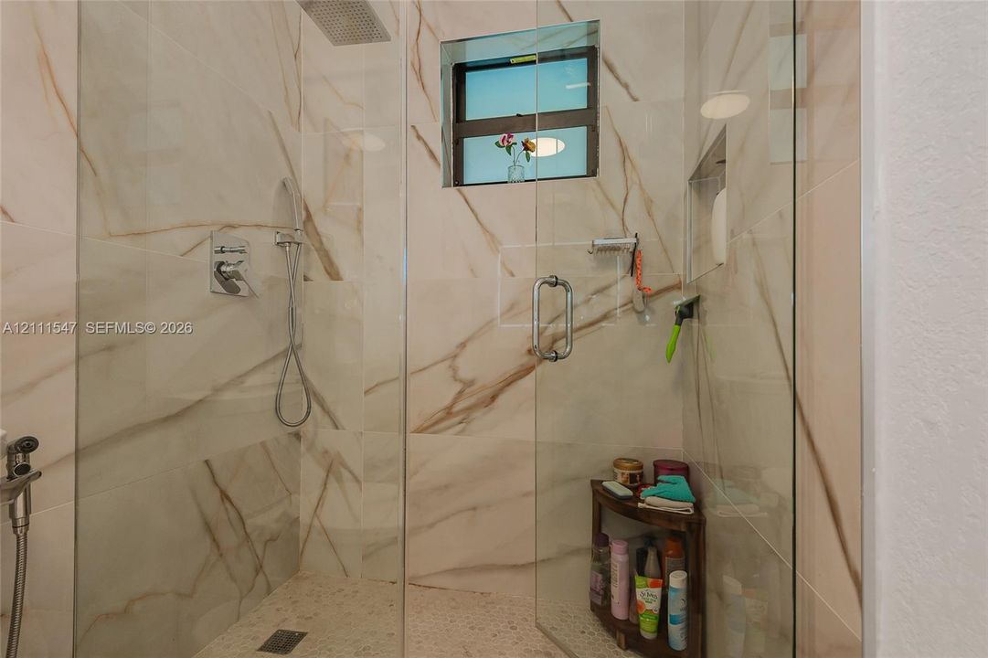Walk-in shower featuring floor-to-ceiling large-format tile, frameless glass enclosure, ceiling-mounted rainfall showerhead, handheld shower fixture, and a built-in recessed niche