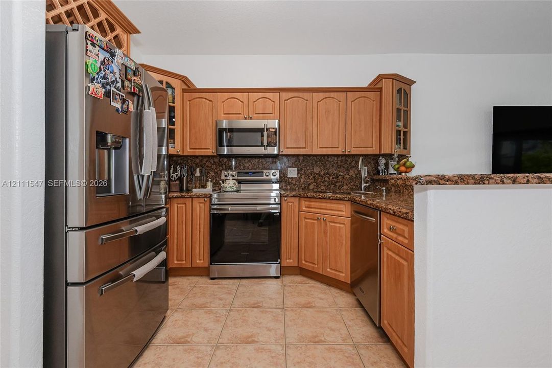 Kitchen featuring natural wood cabinetry, stone countertops, stainless steel appliances, tile flooring, and integrated wine rack storage