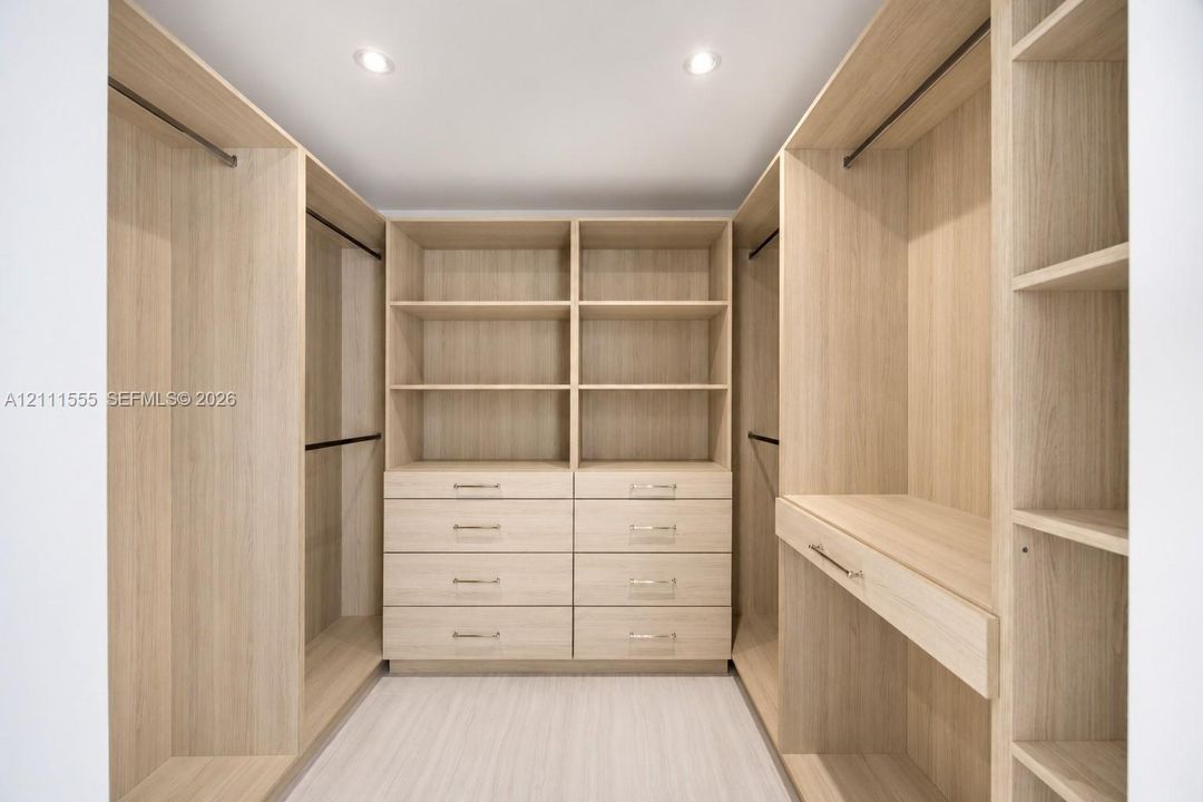Primary Closet - His Custom wood-finish cabinetry featuring integrated shelving, dual hanging rods, built-in dresser drawers with metallic hardware, and recessed ceiling lighting