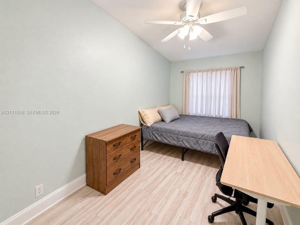 Room featuring wood-finish flooring, a ceiling fan with integrated lighting, and a window with rod-mounted hardware