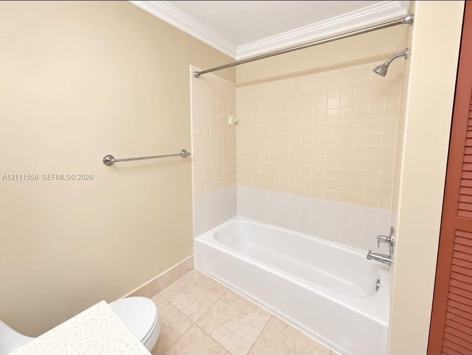 Bathroom featuring a porcelain tub with tile surround, stainless steel shower fixtures, neutral tile flooring, and a stone-surface vanity