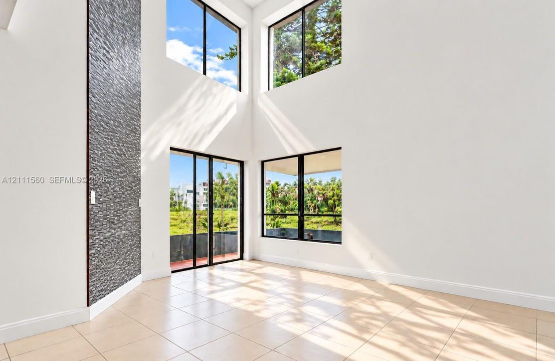 Double-height ceilings featuring floor-to-ceiling windows, a stacked stone accent wall, large format tile flooring, and glass sliding doors