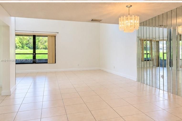 Spacious living area featuring large-format tile flooring, a floor-to-ceiling mirrored wall, a multi-tiered crystal chandelier, and oversized windows