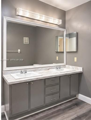 Dual-sink vanity featuring a light-toned stone-patterned countertop, charcoal-toned cabinetry with integrated storage drawers, a large framed wall mirror, and a linear overhead light fixture