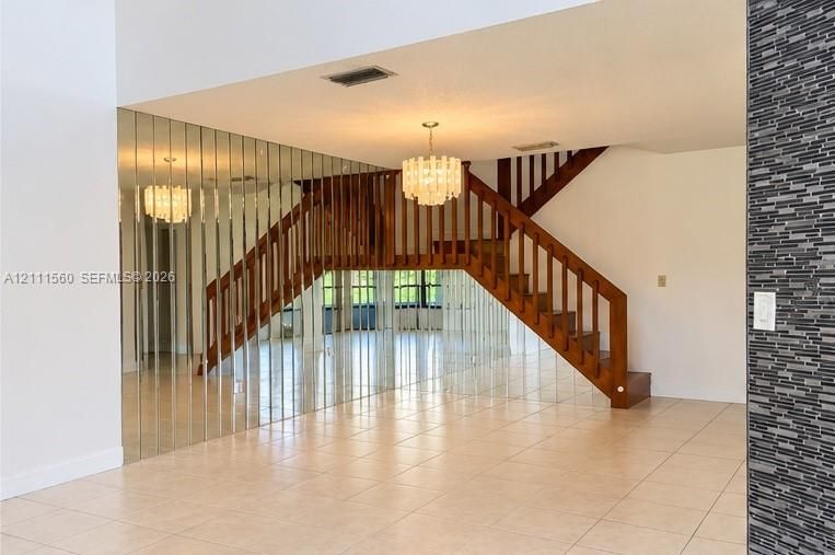 Staircase featuring wood railings and vertical balusters, mirrored accent wall, tiled flooring, tiered glass chandelier, and textured stone-finish wall accent