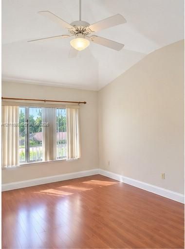 Vaulted ceilings, wood-finish flooring, and a central ceiling fan with an integrated light fixture, complemented by large windows with horizontal blinds