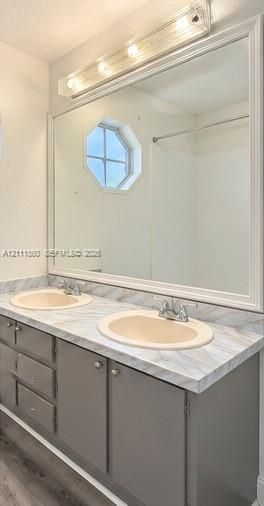 Double vanity featuring solid-surface countertops with integrated dual sinks, gray shaker-style cabinetry, a large framed vanity mirror, and a geometric-shaped window